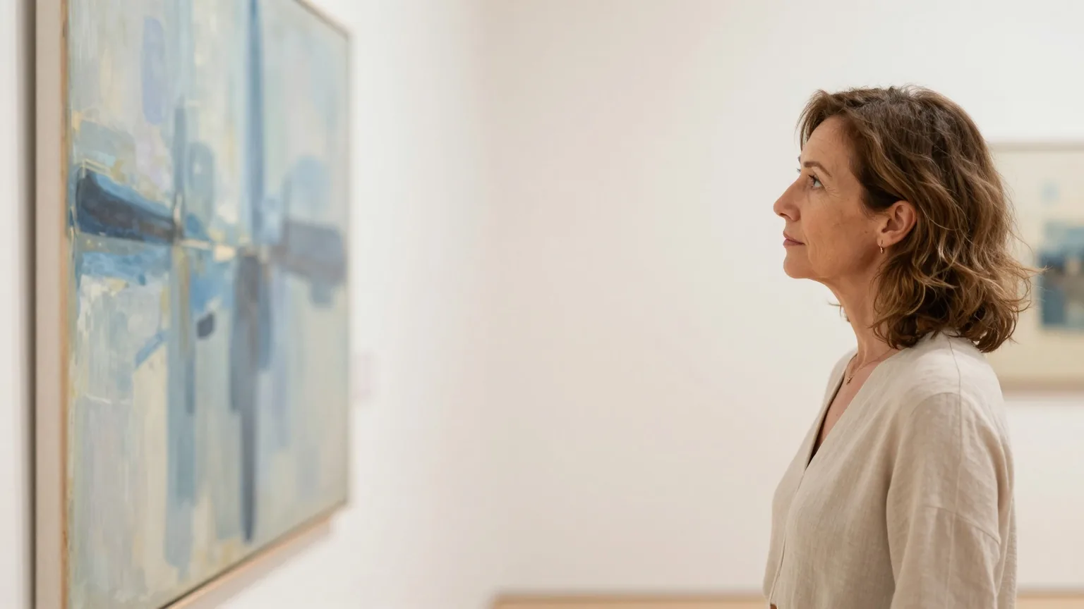 Frau in den Fünfzigern betrachtet in einer ruhigen, hellen Galerie ein großes Gemälde