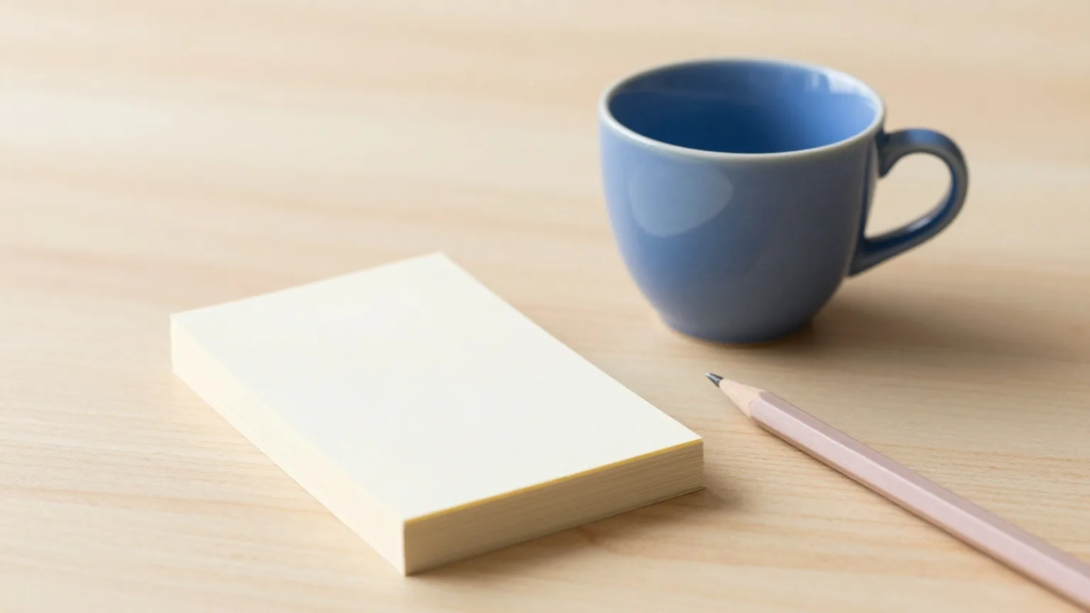 Kleiner Stapel leerer Karteikarten mit Bleistift neben einer indigoblauen Tasse auf einem hellen Holztisch